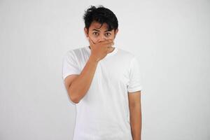 portrait de effrayé Jeune asiatique homme couvrant bouche avec mains portant blanc t chemise isolé sur blanc Contexte photo