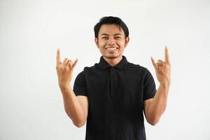 souriant Jeune Beau asiatique homme portant noir polo t chemise et en criant avec fou expression Faire geste Roche symbole avec mains en haut. la musique étoile. lourd concept. isolé sur blanc Contexte photo