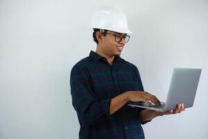 Jeune asiatique architecte homme portant constructeur sécurité casque plus de isolé Contexte Faire content avec en portant portable avec main. photo
