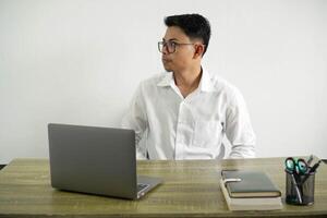 Jeune asiatique homme d'affaire dans une lieu de travail fabrication les doutes geste à la recherche côté, portant blanc chemise avec des lunettes isolé photo