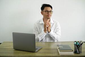 Jeune asiatique homme d'affaire dans une lieu de travail intrigant quelque chose, portant blanc chemise avec des lunettes isolé photo