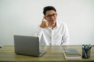 Jeune asiatique homme d'affaire dans une lieu de travail fabrication téléphone geste avec des doigts. appel moi retour signe, porter blanc chemise avec des lunettes isolé photo