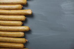 poulet saucisses avec herbes mensonge suivant à chaque autre sur une gris Contexte avec espace pour fond texte. préparation pour une barbecue pique-nique photo