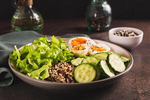 bol avec quinoa, concombre, bouilli œuf, salade et sésame des graines sur le table photo