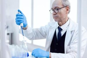 personnes âgées scientifique Faire pharmaceutique expérience en utilisant compte-gouttes pipette. Sénior professionnel chimiste en utilisant pipette avec bleu Solution pour microbiologie essais. photo