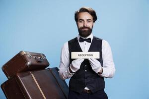 porter guides touristes dans le droite chemin par mettant en valeur accueil symbole sur caméra. qualifié Hôtel portier dans le Voyage industrie, montrer du doigt à enregistrement bureau contre bleu Contexte. photo