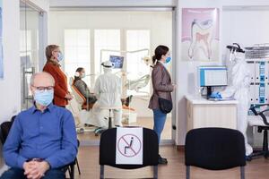 les patients avec protection masque attendre dans stomatologie accueil avec Nouveau normal, Personnel portant ppe costume. femme vérification rendez-vous avec infirmière à venir pour dentaire contrôle pendant coronavirus pandémie photo