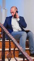 surmené fatigué homme d'affaire en train de lire projet date limite pendant téléphone appel avec entreprise directeur. sérieux entrepreneur travail sur emploi séance sur escalier de affaires bâtiment en retard à nuit. photo