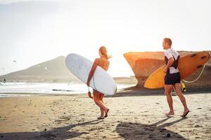 surfeurs couple fonctionnement ensemble avec planches de surf sur le plage à le coucher du soleil - sportif copains ayant amusement Aller à le surf - voyage, vacances, sport mode de vie concept photo