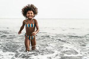 afro enfant ayant amusement en jouant à l'intérieur mer l'eau pendant été vacances. enfance et Voyage vacances concept ré photo