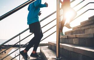 vue de coureurs jambes formation Extérieur - Jeune couple Faire une faire des exercices session sur escaliers suivant le plage à le coucher du soleil - en bonne santé personnes, le jogging et sport mode de vie concept photo