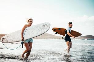 surfeurs couple fonctionnement ensemble avec planches de surf sur le plage à le coucher du soleil - sportif copains ayant amusement Aller à le surf - voyage, vacances, sport mode de vie concept photo