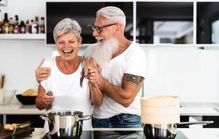 content Sénior couple ayant amusement cuisine ensemble à Accueil - personnes âgées gens en train de préparer santé le déjeuner dans moderne cuisine - retraité mode de vie famille temps et nourriture nutrition concept photo