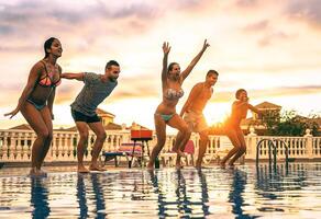 groupe de content copains sauter dans le bassin à le coucher du soleil - Jeune gens ayant amusement fabrication fête dans exclusif recours tropical dans vacances - concept de amitié, vacances et jeunesse mode de vie photo