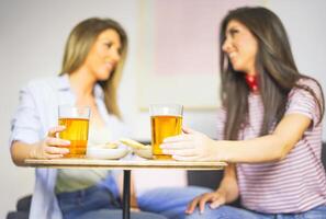 Jeune femmes profiter une repas en buvant Bière et en mangeant Pizza à Accueil - content copains ayant amusement avec une le déjeuner dans leur appartement séance sur canapé - amitié, nourriture, mode de vie concept photo