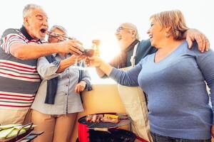 content Sénior copains ayant amusement applaudissement avec rouge du vin à barbecue dans terrasse Extérieur - mature gens à manger et en riant ensemble sur toit - relation amicale et personnes âgées mode de vie concept photo