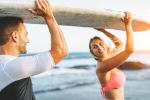 content aimant couple en portant une planche de surf et à la recherche chaque autre - copains ayant amusement surfant pendant une vacances - gens relation, voyage, des sports mode de vie concept photo