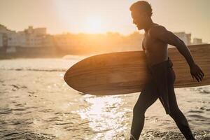 Masculin afro surfeur ayant amusement surfant pendant le coucher du soleil temps - africain homme profiter le surf journée - extrême sport mode de vie gens concept photo