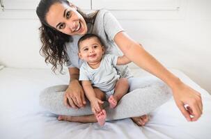 content mère ayant amusement avec sa peu bébé sur lit - famille et maternité concept photo