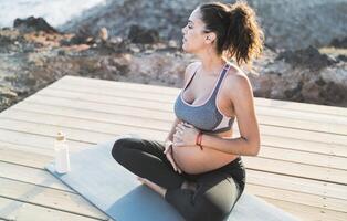 content Jeune femme caressant sa Enceinte ventre tandis que Faire yoga Extérieur - santé mode de vie et maternité concept photo