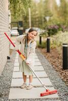 une peu fille avec une brosse nettoie une chemin sur le rue dans le Cour photo