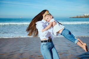 content Jeune mère pièces avec sa mignonne enfant sur le plage, en riant et tournant autour, en quittant pas sur le humide le sable photo