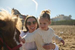 content mère porter sa fille tandis que caressant une peu poney Extérieur photo