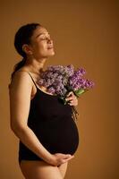 délicieux Enceinte femme, femme enceinte mère caressant sa ventre, en portant violet lilas, isolé beige studio Contexte photo
