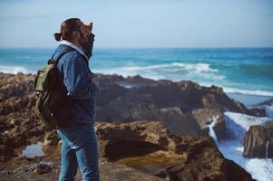 personnes. actif mode de vie. Jeune voyageur aventurier gars avec sac à dos, à la recherche dans distance, permanent sur le falaise. photo