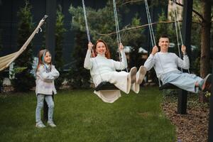 maman et papa sont équitation sur une balançoire et là est une fille permanent suivant à eux. le famille est repos sur une balançoire photo