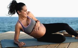 content Jeune femme caressant sa Enceinte ventre tandis que Faire yoga suivant le océan - santé mode de vie et maternité concept photo