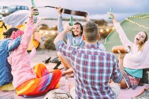 content copains fabrication fête en buvant bières et en jouant la musique tandis que camping avec tentes Extérieur - Jeune gens ayant amusement et en riant ensemble - amitié, fête, camp, mode de vie concept photo