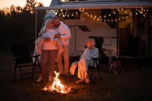 le famille est relaxant ensemble par le feu de camp près leur mobile maison. soir famille vacances photo