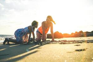 content aimant famille en jouant sur le plage pendant une magnifique le coucher du soleil - mère et fille ayant amusement profiter temps ensemble et dessin dans le le sable - parent, enfance et maternel l'amour concept photo