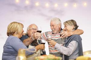 content Sénior copains grillage avec rouge du vin à barbecue dîner dans terrasse - mature gens à manger et applaudissement ensemble en buvant du vin sur toit - relation amicale et personnes âgées mode de vie concept photo