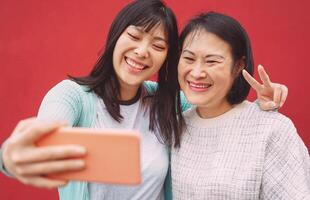 asiatique mère et fille prise photo selfie avec mobile téléphone intelligent Extérieur - content chinois famille ayant amusement avec Nouveau les tendances La technologie applications pour social médias - gens La technologie mode de vie concept