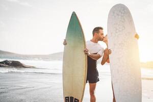content couple de surfeur embrasser avant à aller à le surf - sportif gens ayant une soumissionner moment sur le plage à le coucher du soleil - concept de sport mode de vie, extrême, l'amour et relation photo