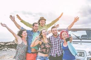 groupe de content copains prise une selfie en utilisant mobile intelligent téléphone pendant une route voyage avec jeep voiture - Voyage gens ayant amusement diffusion mains en haut tandis que prise soi Photos dans désert - esprit d'aventure concept