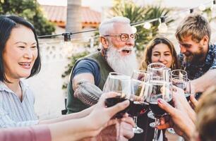 content famille applaudissement et grillage avec rouge du vin des lunettes à dîner Extérieur - gens avec différent âge et l'ethnie ayant amusement à un barbecue fête - nourriture et boire, retraité et Jeune gens concept photo