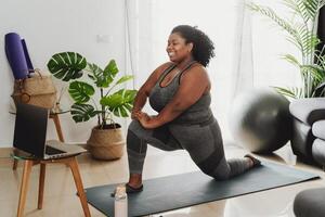 Jeune africain femme prise une virtuel pilates aptitude classe avec portable à Accueil - sport bien-être gens mode de vie concept photo