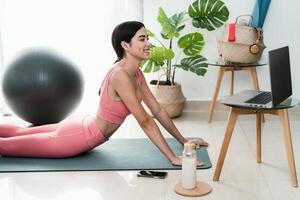 Jeune Latin femme Faire pilates virtuel aptitude classe avec portable à Accueil - sport bien-être gens mode de vie concept photo