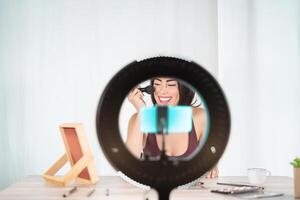 Jeune femelle vlogger Faire maquillage Didacticiel vidéo pour la toile canal à Accueil - content influenceur fille ayant amusement tournage avec mobile téléphone intelligent - social médian et millénaire génération mode de vie concept photo