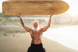 Sénior Masculin ayant amusement surfant pendant le coucher du soleil temps - en forme retraité homme formation avec planche de surf sur le plage - personnes âgées en bonne santé gens mode de vie et extrême sport concept photo