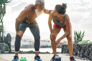 en forme couple ayant une Pause après une vite course suivant le plage à le coucher du soleil - sportif gens faire des exercices fonctionnement Extérieur - aptitude, bien-être, sport, le jogging et santé mode de vie concept photo