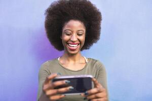 content afro fille en utilisant mobile téléphone intelligent Extérieur - souriant social influenceur femme ayant amusement avec Nouveau les tendances La technologie applications - gens technologie dépendance et médias mode de vie concept - violet Contexte photo