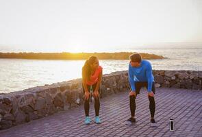 santé Jeune couple prise une Pause de courir ensemble suivant le océan pendant une magnifique le coucher du soleil - gens travail en dehors sur le plage - relation, sport, mode de vie concept photo