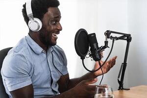 africain homme enregistrement une Podcast en utilisant microphone et écouteurs de le sien Accueil studio photo