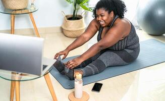 Jeune africain courbée femme Faire pilates en ligne aptitude classe avec portable à Accueil - sport bien-être gens mode de vie concept photo