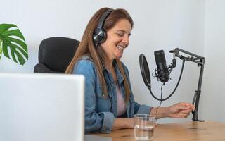 mature femme enregistrement une Podcast en utilisant microphone et portable de sa Accueil studio photo