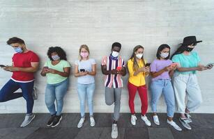 Jeune gens portant visage masque en utilisant mobile téléphone intelligent Extérieur - multiracial copains ayant amusement avec Nouveau La technologie social médias app pendant couronne virus déclenchement - jeunesse millénaire mode de vie concept photo